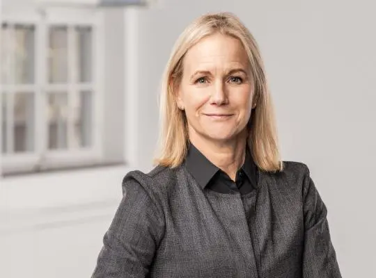 Mika Romanus Konstnärsnämndens direktör lätt vriden leende Mika står lätt vriden och tittar leende in i kameran. Man ser överkroppen och ett fönster i bakgrunden. Fotografiet är i färg.