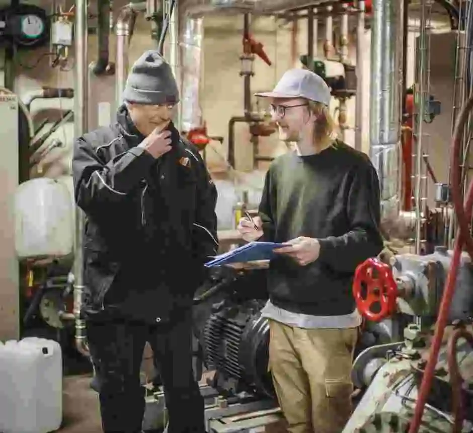 Två män står i en ishalls maskinrum och för ett samtal.