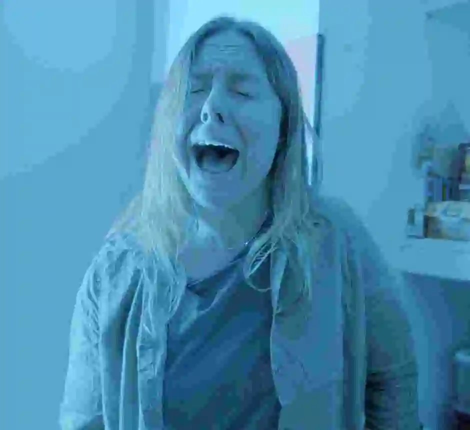 Blond kvinna blundar och sjunger i ett kök avbildat med blått filter.
