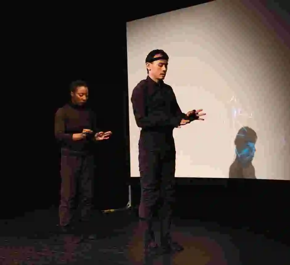 Två personer helt klädda i svart står i djup kontemplation framför en filmduk.