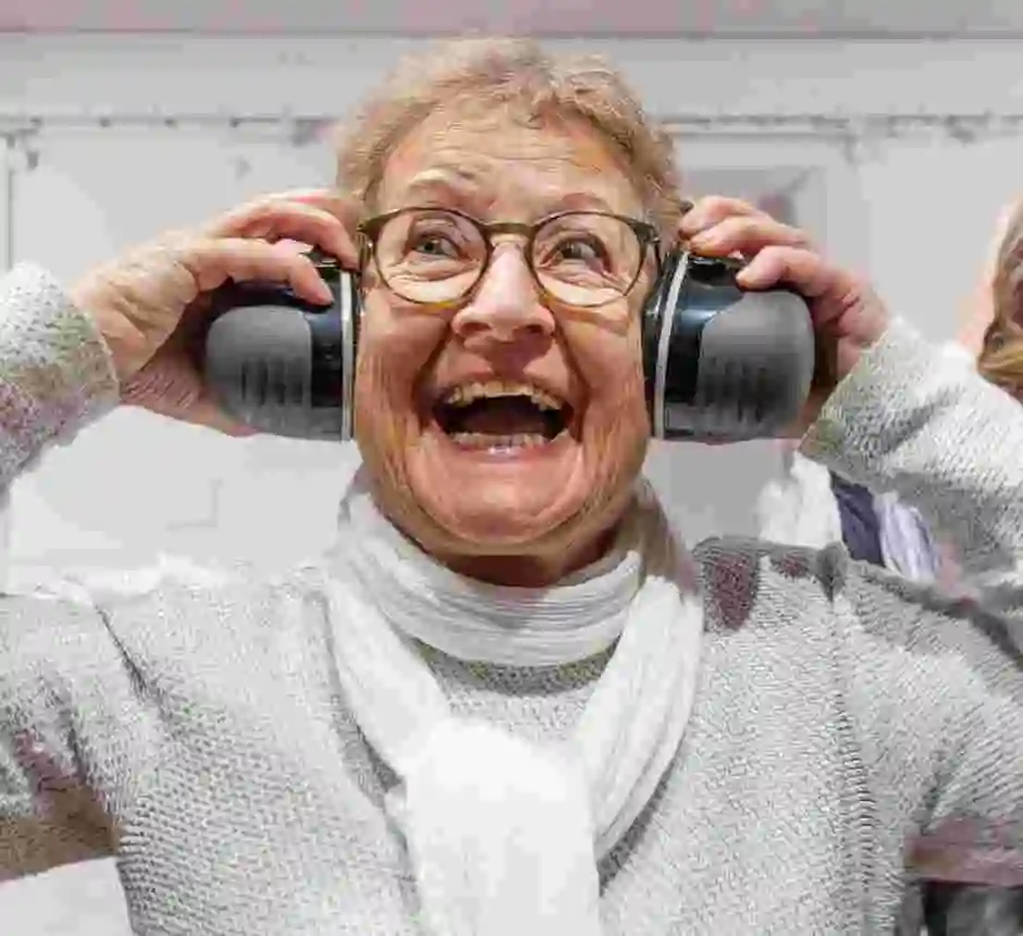 Brett leende äldre kvinna lyssnar ur stora hörlurar.