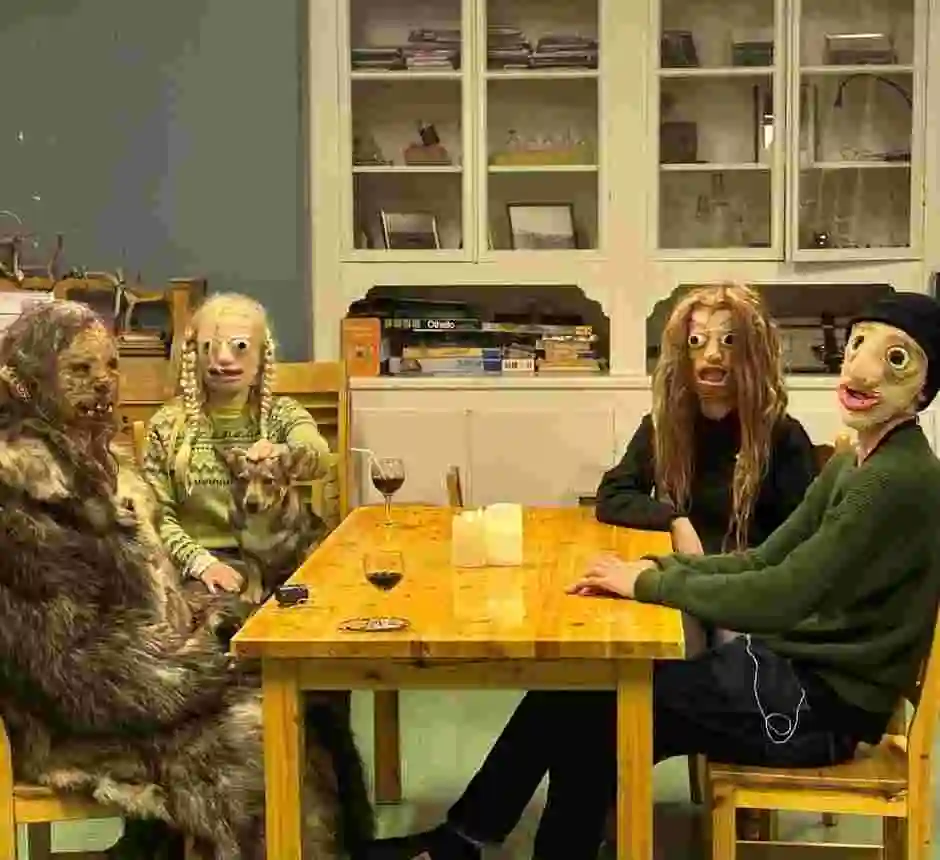 Fyra personer i masker, varav en med en hund i knät, sitter runt ett bord och tittar in i kameran.