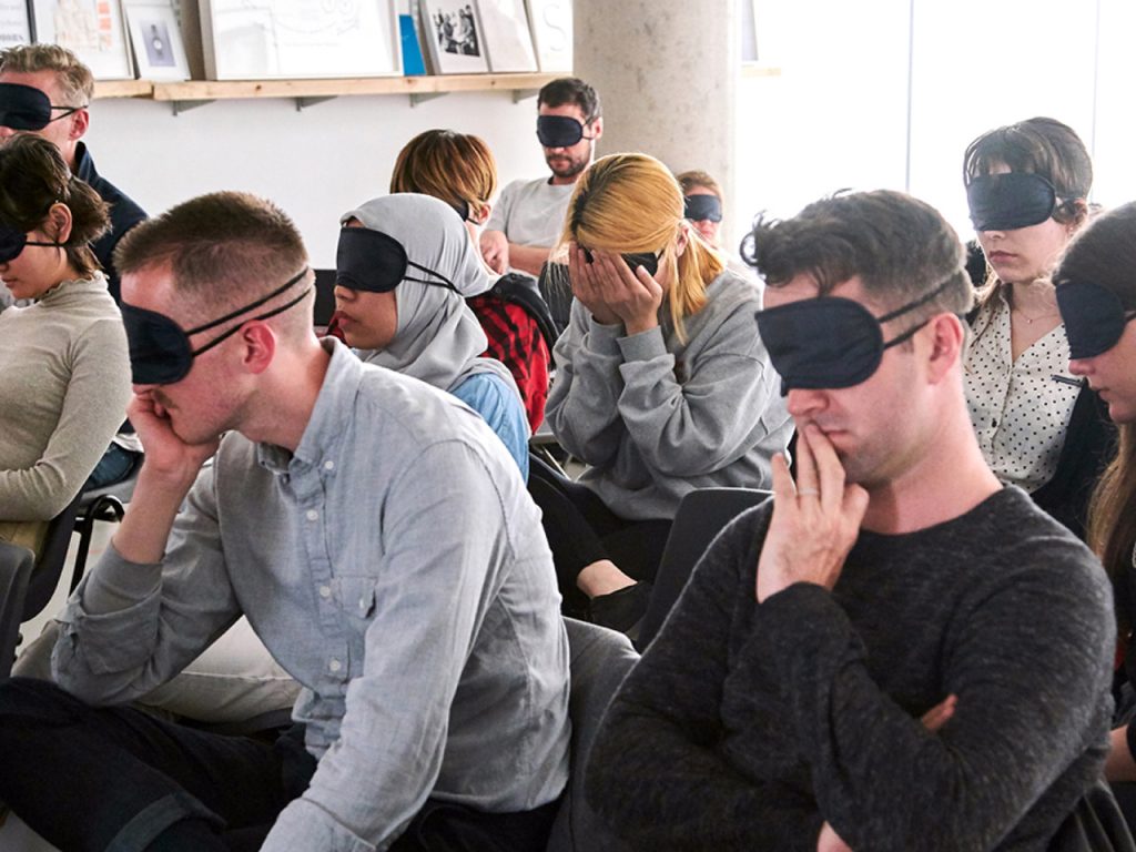 People sitting on chairs listening blindfolded