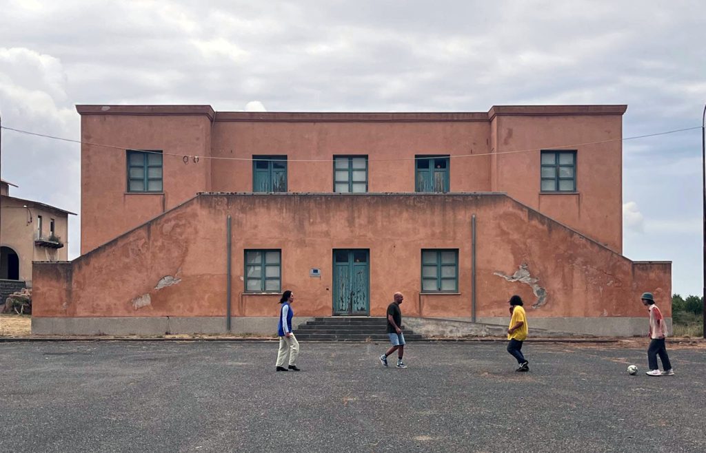 Personer spelande fotboll framför en byggnad i fascistisk stil 