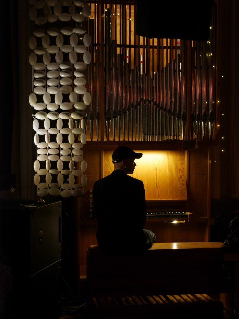 Musikkonstnären Arvid Kraft sitter framför en orgel i dunkel belysning.